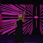 Mary J. Blige performing on stage with a microphone, arm raised