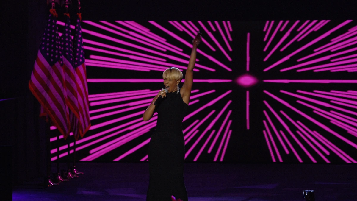 Mary J. Blige performing on stage with a microphone, arm raised